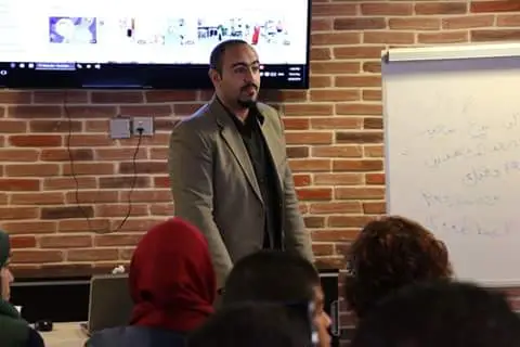 حسن الحلبي في قاعة تدريب أمام شاشة العرض
