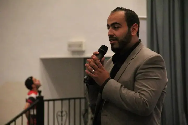 حسن الحلبي متحدثاً بالميكروفون في ندوة